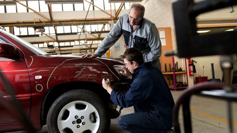 A specialist outlining the damaged area during fender repair at the car body shop